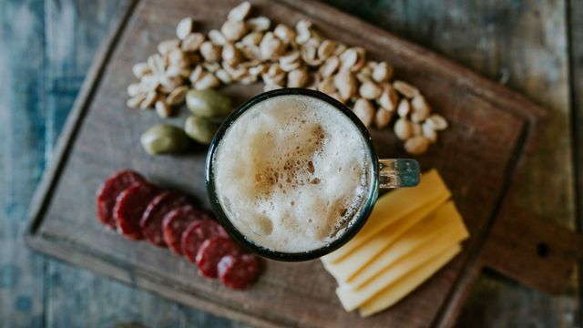 A top-down photo of a beer on a board with cheese, meat and nuts. 