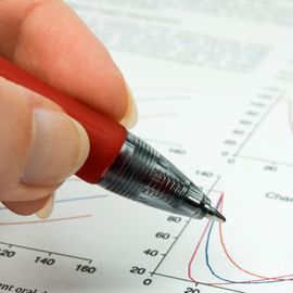 A person's hand holding a pen poised over a graph in a scientific paper. 